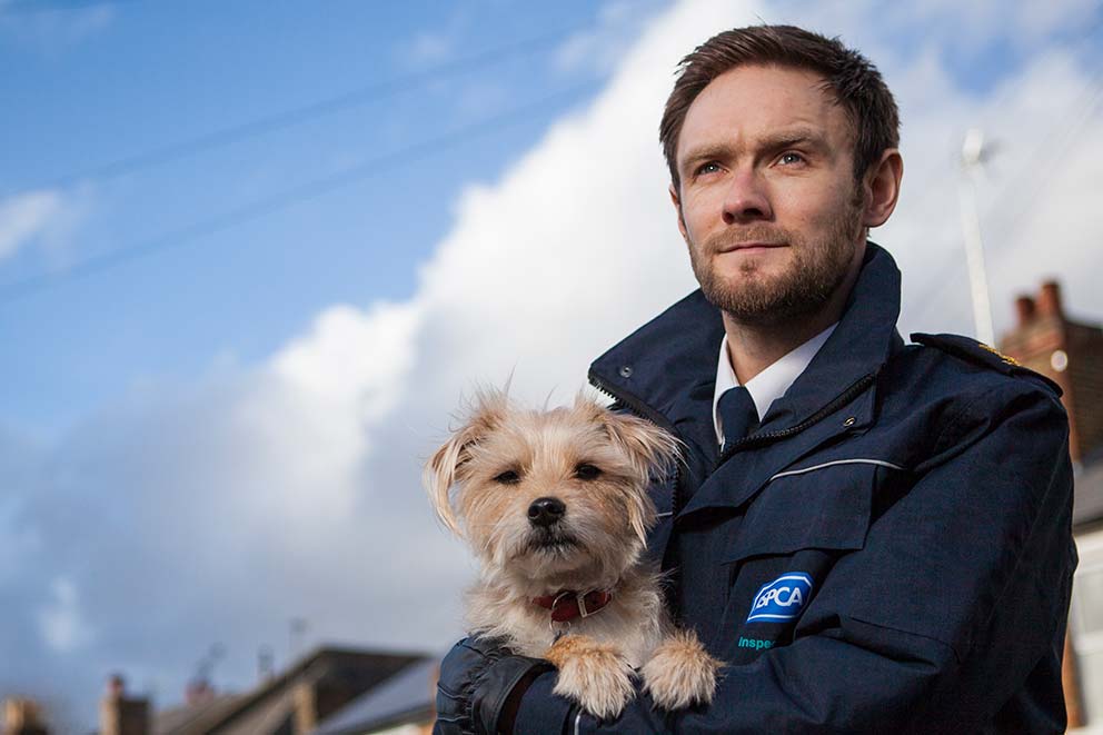An RSPCA inspector standing outside holding a dog.